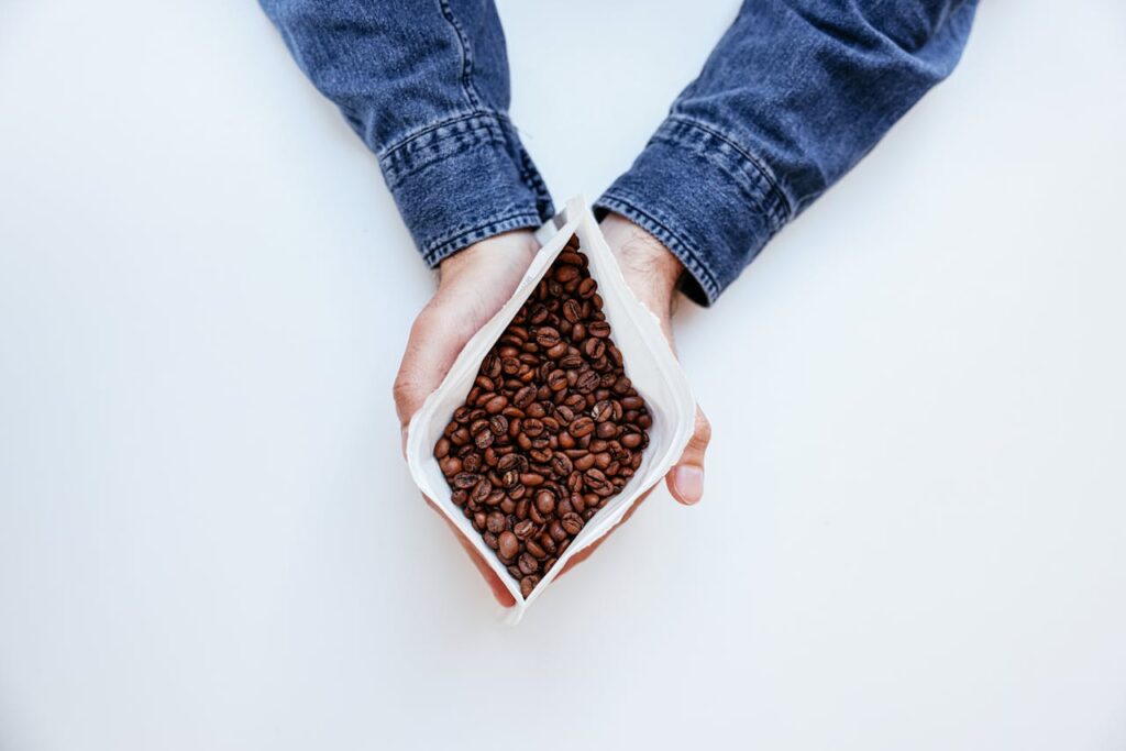 Top view of a person holding a paper bag filled with coffee beans, set against a white background.